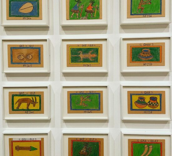 Parete con dodici disegni incorniciati di Frédéric Bruly Bouabré: pittogrammi colorati su cartoncino con lettere e numeri